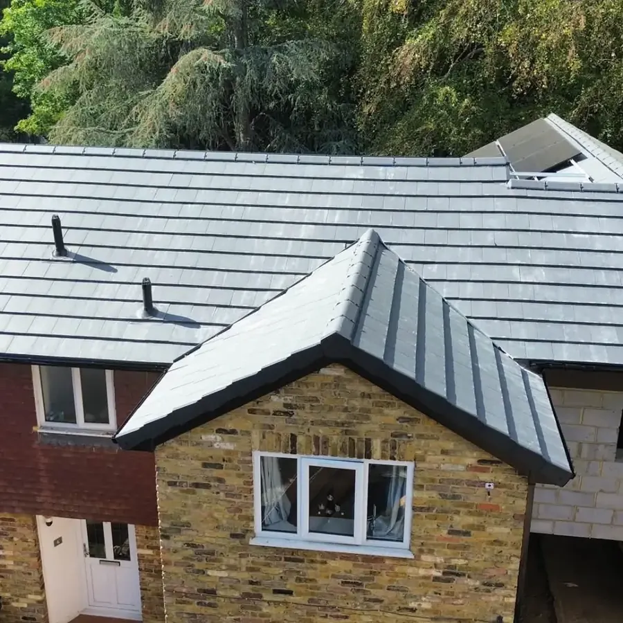 Aerial view of a large grey slate roof with solar panels on a nearby home